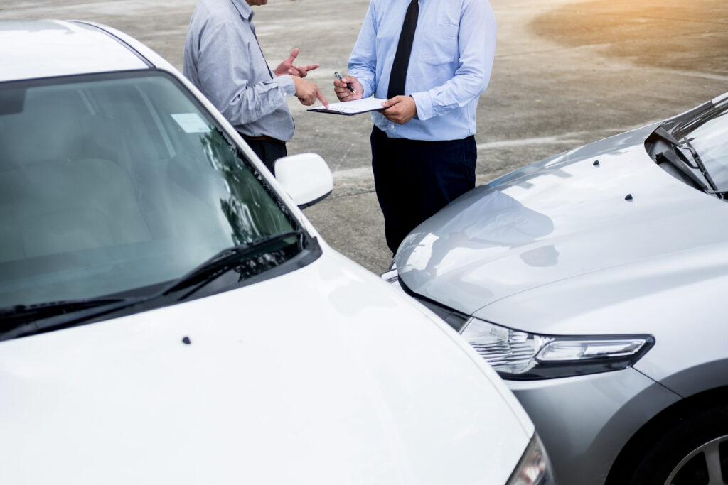 Insurance agent writing on clipboard while examining car after accident claim being assessed and processed.