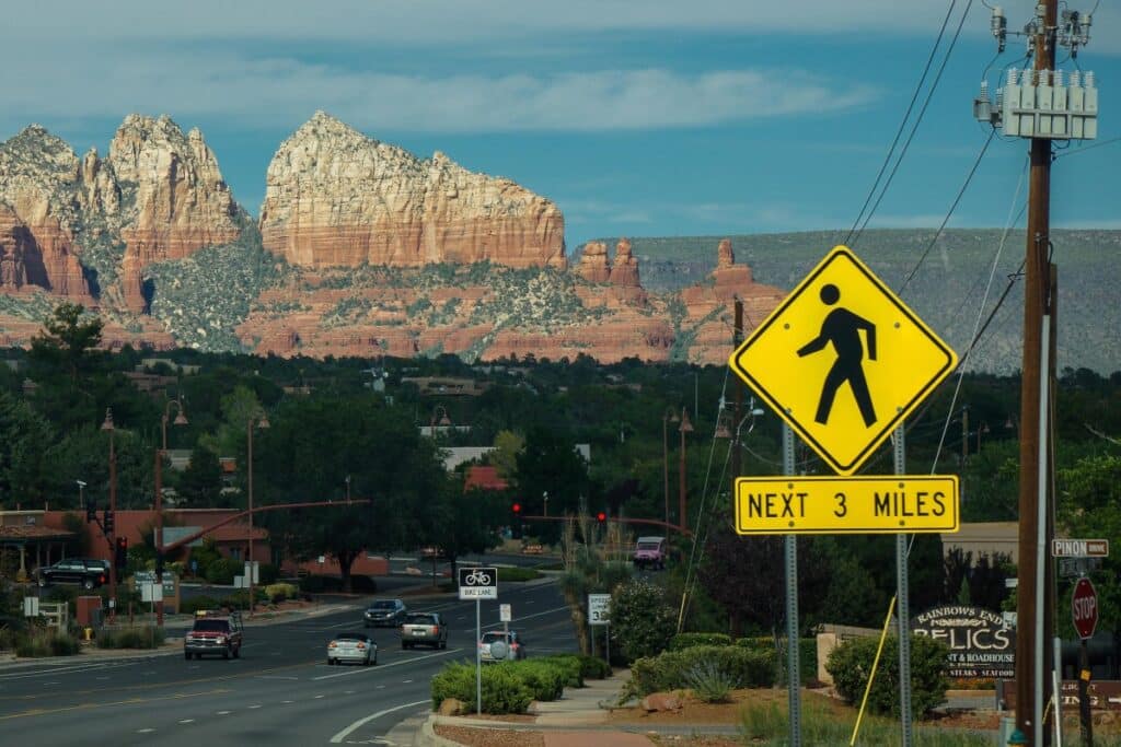 Photo of Pedestrian crossing sign in Sedona, AZ, with a busy roadway and Red Rock Park in background.